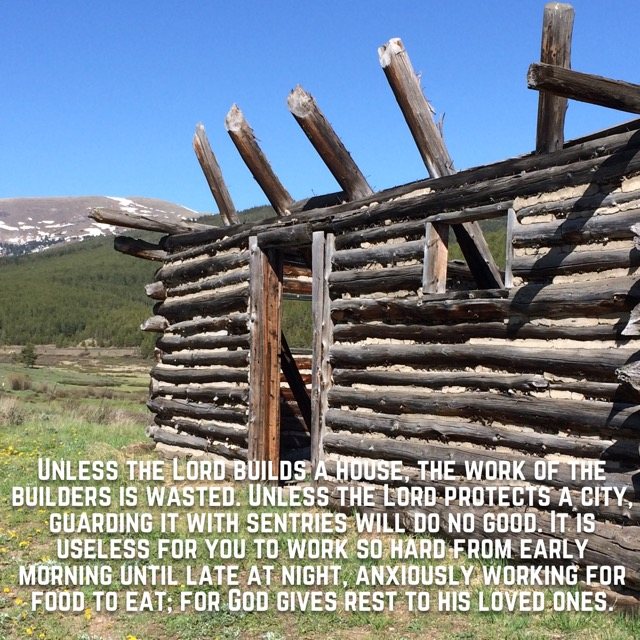 An old log cabin in a high mountain meadow, with the words of Psalm 127:1–2