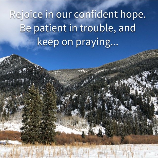 Evergreens below snowy mountain slopes, with the words of Romans 12:12